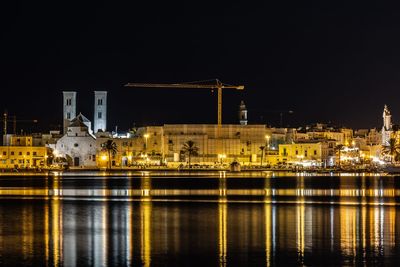 Illuminated buildings by river against sky at night