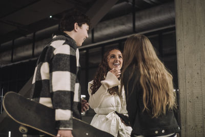 Low angle view of excited girl talking with male and female teenage friends at mall