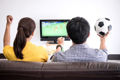 Rear view of men and women watching match on sofa at home