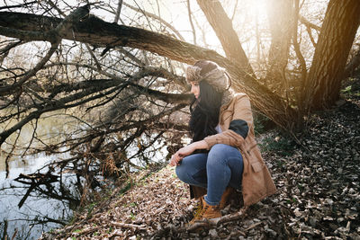 Woman sitting by bare tree in forest