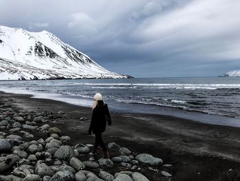 Rear view of woman on beach against sky during winter