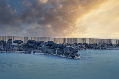 Stones at geothermal spa in blue lagoon against cloudy sky during sunset