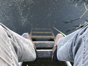 Low section of man sitting on ladder in pond