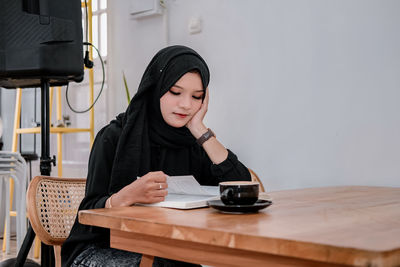 Young woman using mobile phone while sitting on table