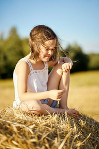 Cute little girl sits on mown rye in the field in summer