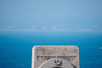 Information sign by sea against blue sky