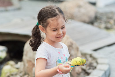 Cute girl holding a tame bird on a feed stick at the zoo