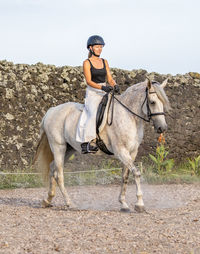 White lusitano mare, female dressage rider, outdoors on sand.