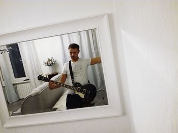 Reflection of man playing guitar at home