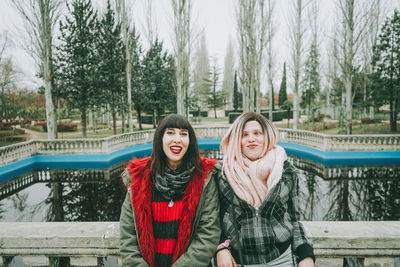 Portrait of smiling friends leaning on railing against lake during winter