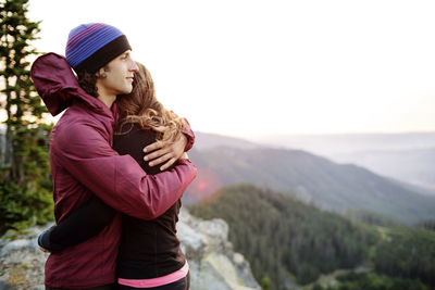 Couple embracing while standing on top of mountain against clear sky