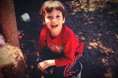 Portrait of smiling boy crouching by tree