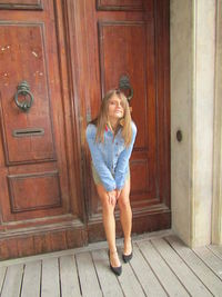 Portrait of smiling young woman standing against door