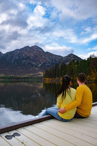 People sitting on lake by mountains against sky