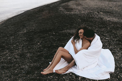 A couple in love spend the night at the sea, kissing and hugging on the beach covered with a blanket