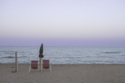 Chairs on beach against sky during sunset