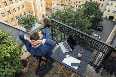 Male business person with hands behind head sitting in office balcony