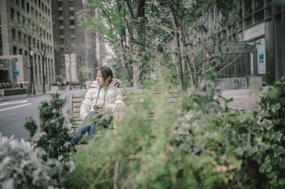 Woman looking away while sitting on bench in city