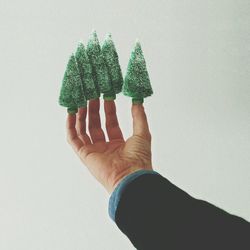 Close-up of christmas trees on fingertips over white background
