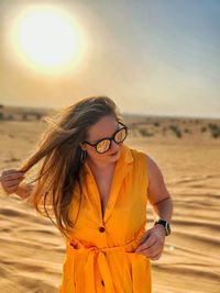 Young woman wearing sunglasses standing at desert against sky