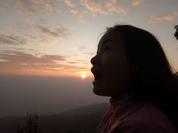 Woman shouting while looking away against sky during sunset