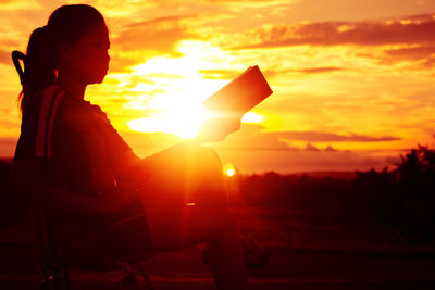 Side view of silhouette man sitting against orange sky
