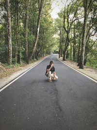 Full length of man crouching on road against trees