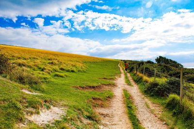 Dirt road amidst field against sky