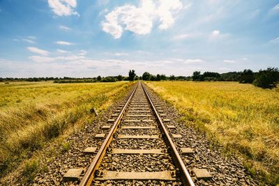 Railroad track amidst grassy field against cloudy sky