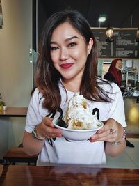 Portrait of smiling woman holding bowl with dessert at cafe
