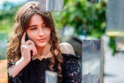 Smiling young woman listening over phone while sitting at sidewalk cafe