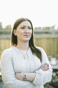 Thoughtful woman standing arms crossed outdoors