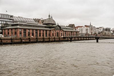 View of buildings by river against cloudy sky