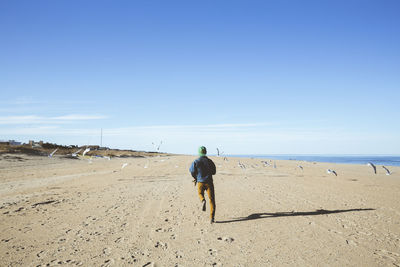 Full length rear view of man running on beach against blue sky