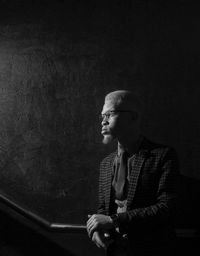 Thoughtful man looking away while standing against wall in darkroom