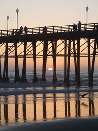 Silhouette bridge over sea against clear sky during sunset