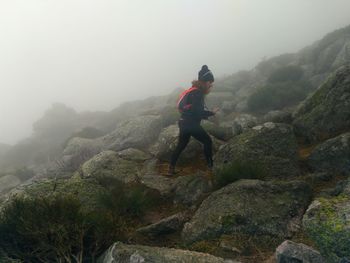Side view of woman walking on rocky mountain during foggy weather