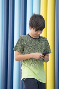 Portrait of a young boy using smartphone walking on coloured background. immersed technology concept