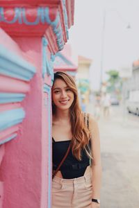 Portrait of young woman standing by wall in city