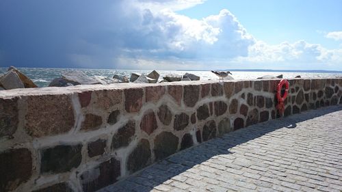 Woman standing on retaining wall by sea against sky