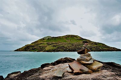 Scenic view of sea by mountain against sky