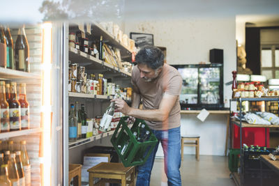 Male employee arranging bottle on shelf in deli