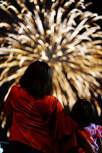 Rear view of woman with daughter enjoying firework display at night