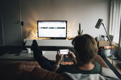 Full length of man using mobile phone while sitting on sofa in living room