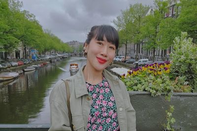 Portrait of young woman standing against river