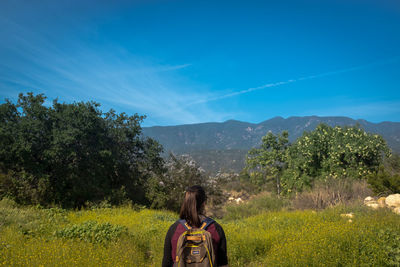 Rear view of backpack woman standing in front of plants and mountains