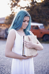 Close-up of young woman holding books while standing on footpath