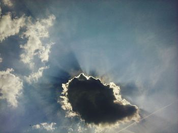 Low angle view of sunlight streaming through clouds