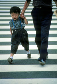 Full length of friends walking on zebra crossing in city