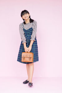 Full length portrait of woman standing against pink background